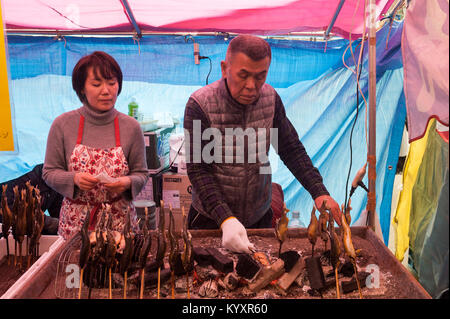 31.12.2017, Tokyo, Giappone, Asia - un uomo prepara appena tostato gli spiedini di pesce in una bancarella di strada a Tokyo il quartiere Shibuya. Foto Stock