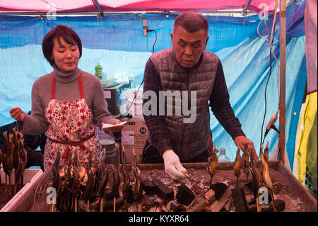 31.12.2017, Tokyo, Giappone, Asia - un uomo prepara appena tostato gli spiedini di pesce in una bancarella di strada a Tokyo il quartiere Shibuya. Foto Stock