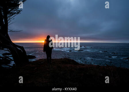 Silhouette ragazza adolescente guardando vista dal mare contro il cielo nuvoloso durante il tramonto Foto Stock