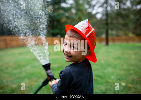 Ritratto di ragazzo che indossa il casco durante la spruzzatura di acqua con tubo flessibile da giardino in cortile Foto Stock