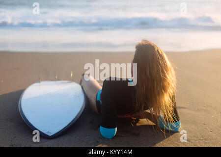 Vista posteriore della donna rilassante da tavola da surf in spiaggia durante il tramonto Foto Stock