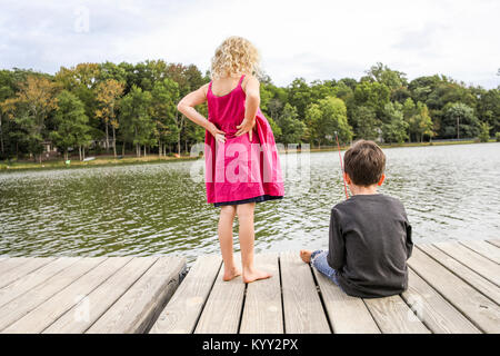 La ragazza con le mani sul hip guardando amico pesca nel lago Foto Stock