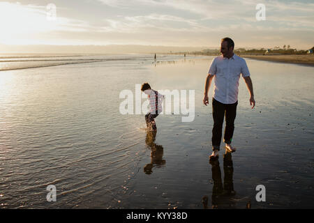 Padre guardando il figlio saltando in acqua sulla riva presso la spiaggia contro sky Foto Stock