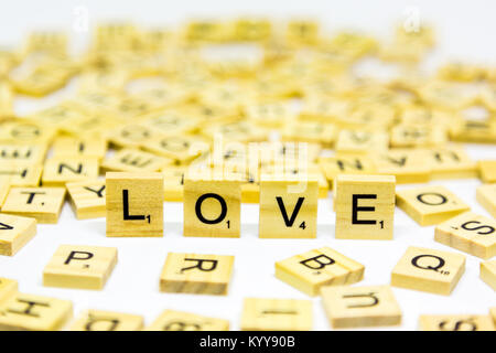 La parola amore in piedi realizzato da legno lettere di scrabble su sfondo bianco Foto Stock