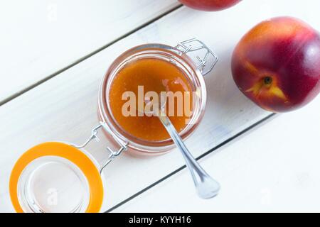 Vista dall'alto in basso su aprire un barattolo di vetro pieno di confettura di pesche Foto Stock
