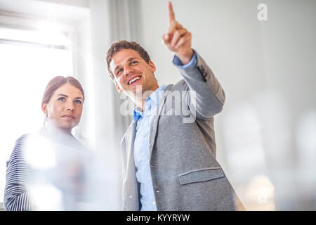 Felice giovane impreditore mostrando qualcosa al collega di sesso femminile in office Foto Stock