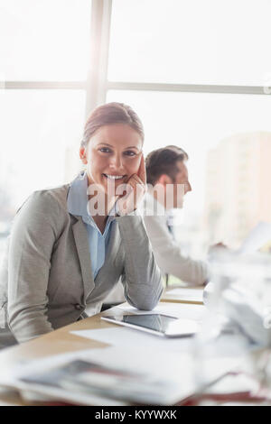 Ritratto di donna sorridente architetto seduto alla scrivania con il collega in background Foto Stock