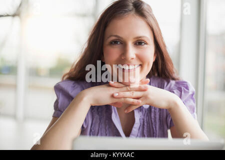 Ritratto di sorridente giovane imprenditrice con le mani sul mento in ufficio Foto Stock