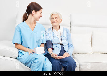 Giovane assistente di infermieristica e senior citizen come un paziente nella misurazione della pressione sanguigna per la prevenzione Foto Stock