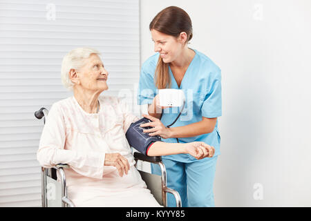 Giovani caregiver misura la pressione del sangue di un'anziana donna anziana come un paziente Foto Stock