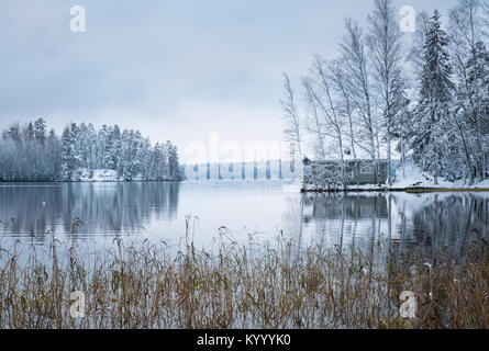 Paesaggio invernale con sauna cottage e tranquillo lago alla sera in Finlandia Foto Stock