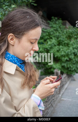 Giovane ragazza è alla ricerca di uno smartphone che tiene nelle sue mani. Foto Stock