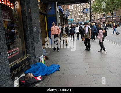 Una persona senza dimora dorme sul marciapiede esterno destro della stazione della metropolitana di Leicester Square su Charing Cross Road nel centro di West End di Londra, 2017 Foto Stock