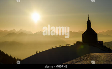 Rottach-Egern, Germania. Xiii gen, 2018. La cappella sul Wallberg la montagna sembra contro la retroilluminazione del sole di setting al Wallberg montagna vicino a Rottach-Egern, Germania, 13 gennaio 2018. Credito: Tobias Hase/dpa/Alamy Live News Foto Stock