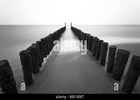 Due file di pali in legno sulla linea costiera in acque mosse creato da una lunga esposizione. Foto Stock