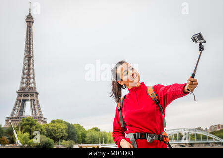 Sorridente giovane donna turistico tenendo selfie con monopiede sullo sfondo della torre Eiffel Foto Stock