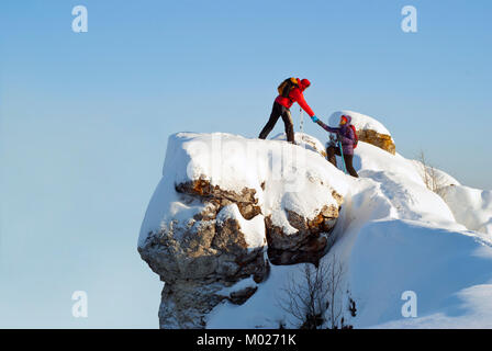 Due escursionisti sulla cima della montagna in inverno; un uomo aiuta una donna a salire su una pietra pura Foto Stock
