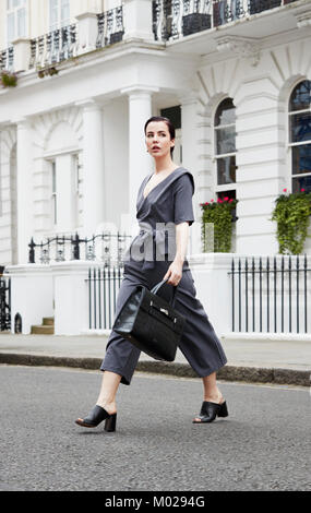 Chic giovane donna in tuta grigio attraversando la London street Foto Stock