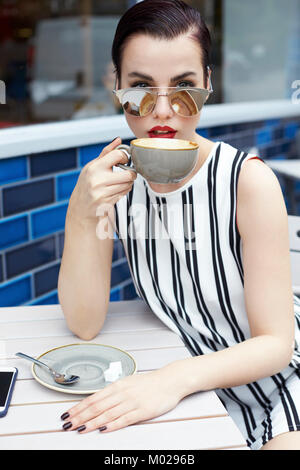 Donna in striped minidress bere fuori cafe, close up Foto Stock