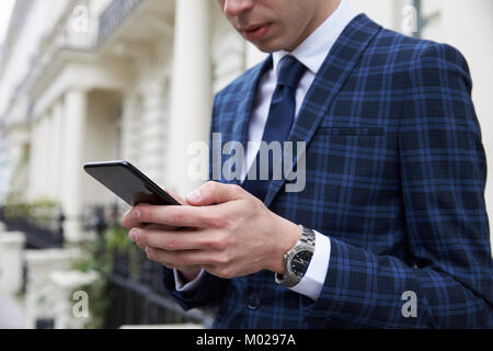 Giovane uomo in tuta controllato usando il telefono in street, metà sezione Foto Stock