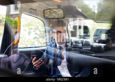 Giovane imprenditore nel retro del London taxi, visto attraverso il vetro Foto Stock