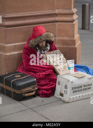 Senzatetto uomo si siede preinstallato su un inverno molto freddo giorno per chiedere aiuto nel distretto finanziario di Lower Manhattan, New York. Foto Stock