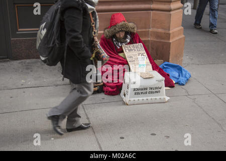 Senzatetto uomo si siede preinstallato su un inverno molto freddo giorno per chiedere aiuto nel distretto finanziario di Lower Manhattan, New York. Foto Stock