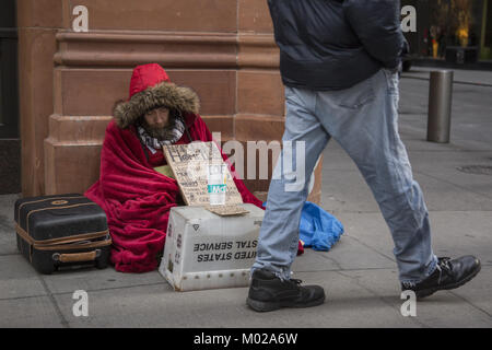 Senzatetto uomo si siede preinstallato su un inverno molto freddo giorno per chiedere aiuto nel distretto finanziario di Lower Manhattan, New York. Foto Stock