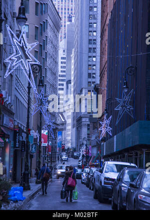 Guardando verso il basso le strette Nassau Street rivestita con decorazioni di vacanza durante la stagione di Natale in Lower Manhattan. New York Stock Exchange picchi thr Foto Stock