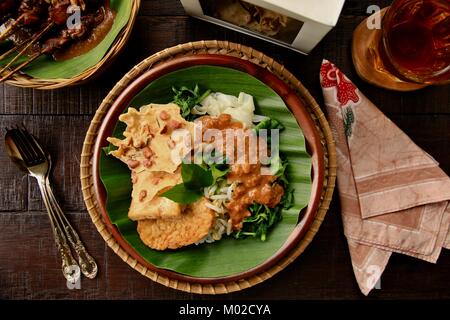 Nasi Pecel, il tradizionale Giavanese piatto di riso di riso al vapore con insalata di verdure, medicazione di arachidi, tempeh e tofu e crackers Foto Stock