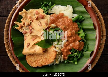 Nasi Pecel, il tradizionale Giavanese piatto di riso di riso al vapore con insalata di verdure, medicazione di arachidi, tempeh e tofu e crackers Foto Stock