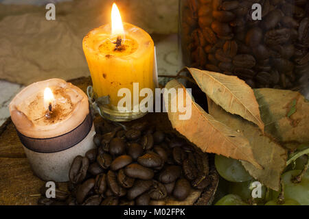 I chicchi di caffè in legno rustico, due candele e foglie secche, autunno Foto Stock