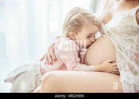 Carino, allegro figlia baciare una madre di ventre Foto Stock