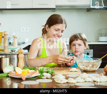 Donna sorridente con un bambino di età superiore rende gnocchi di pesce con salmone all'interno della cucina Foto Stock