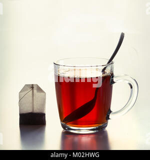 Bicchiere di vetro di acqua calda tè nero e bustine di the sul bianco. Vista laterale. Close up. Foto Stock