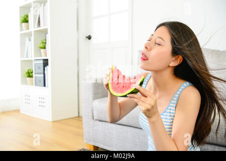 Bella donna graziosa soffia il vento di raffreddamento nel soggiorno e mangiando anguria godendo il tempo di rinfresco durante la stagione estiva. Foto Stock