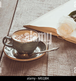 Tazza di caffè nero e libro aperto con rosa bianca sulla tavola di legno. Vintage tonica. Close up. Immagine quadrata. Foto Stock