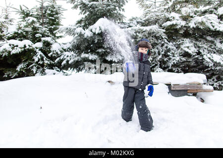 Vista frontale di un bambino in vestiti caldi mirando con una palla di neve a telecamera. Ragazzo avente il divertimento sulla neve. Foto Stock