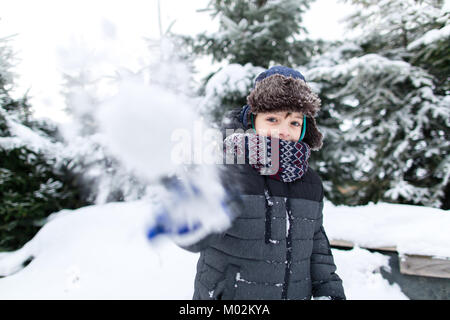 Vista frontale di un bambino felice in vestiti caldi per divertirsi in un giardino innevato, ragazzo avente il divertimento sulla neve. Foto Stock