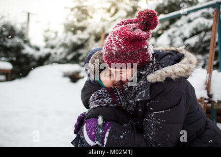 Vista laterale di un felice madre e suo figlio abbraccia ogni altro dopo una lotta con le palle di neve. Famiglia avente il divertimento sulla neve. Foto Stock