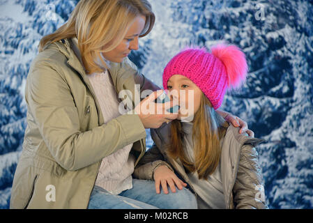 Ragazza con un inalatore per asma dalla sua mano le madri nel periodo invernale Foto Stock