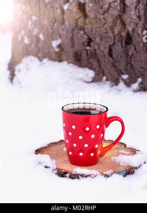 Ceramic red cup con il bianco a pois con caffè nero su un moncone sotto i raggi del sole di sera Foto Stock