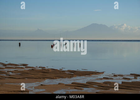 I pescatori locali in piedi sul mare di Alba durante la bassa marea, mantenendo le loro canne da pesca e in attesa di una cattura. Prese ad una spiaggia di Bali, Indonesia. Foto Stock
