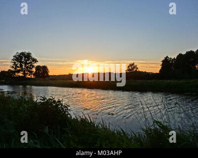Questa fotografia cattura un tramonto sereno sul canale Bydgoszcz in Polonia. L'immagine mette in evidenza l'acqua tranquilla e il paesaggio circostante, offrendo una vista tranquilla della bellezza naturale del canale. Foto Stock