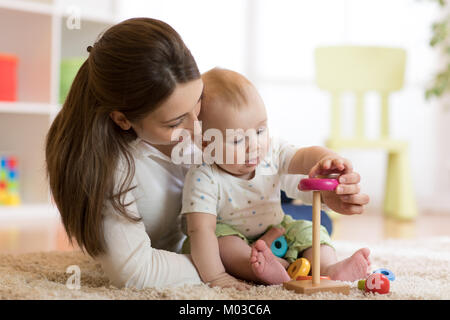 Little baby boy e la sua mamma gioca con i giocattoli a casa Foto Stock