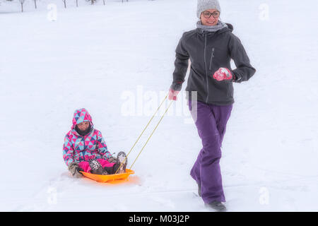 Madre tirando una slitta con la figlia a bordo in inverno Foto Stock