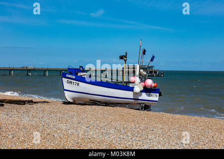 Una piccola barca da pesca cazzate fino sulla spiaggia di trattare nel Kent, il molo in background, REGNO UNITO Foto Stock
