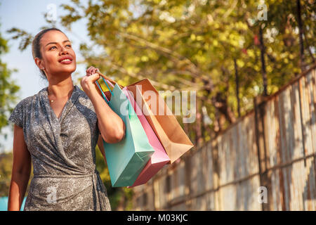 Donna asiatica shopper shopping e colorato di contenimento delle borse per lo shopping in cerca di traverso sulla sinistra e copia di spazio sulla destra con sfondo sfocato Foto Stock