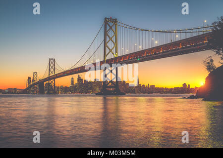 Classic vista panoramica dello skyline di San Francisco con il famoso Oakland Bay Bridge illuminato nel bellissimo golden luce della sera al tramonto in estate Foto Stock