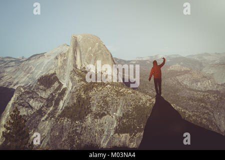 Un giovane escursionista è in piedi su una roccia godendo della vista verso il famoso Half Dome presso il Glacier Point in beautiful Golden luce della sera al tramonto in estate Foto Stock